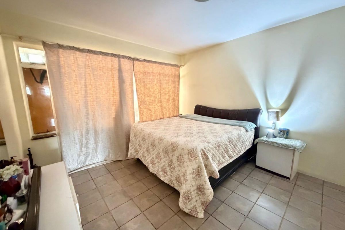 A bedroom featuring tiled flooring and large windows with curtains, providing a functional and well-lit sleeping space.