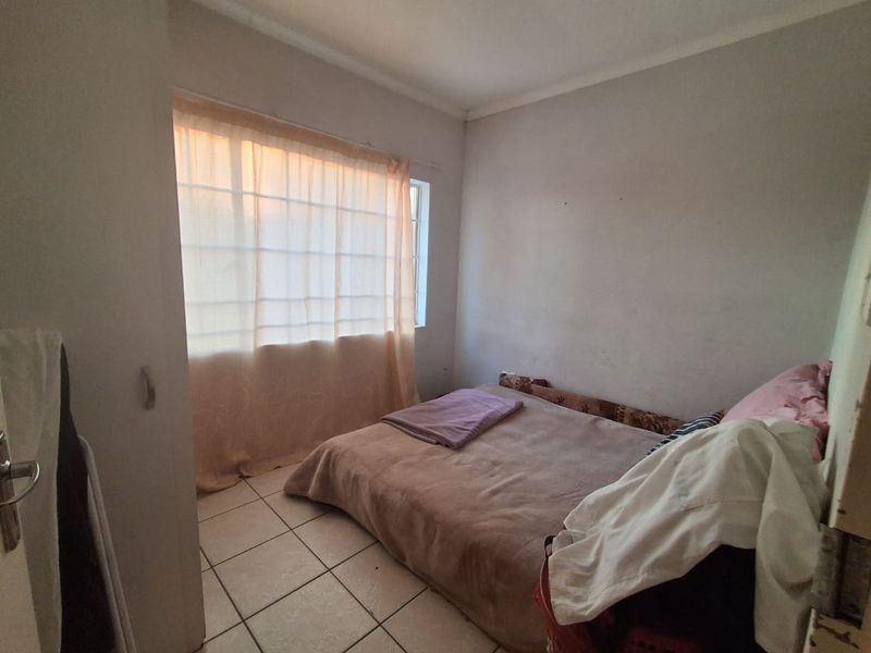 A compact bedroom featuring tiled flooring and a window, currently requiring cosmetic updates to the wall finishes.