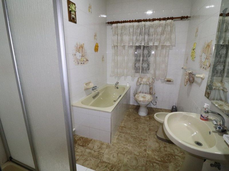 A dated bathroom featuring a built-in bathtub, pedestal sink, bidet, and shower enclosure with original ceramic tiling.