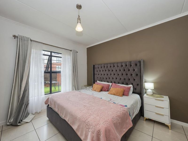 A well-maintained bedroom featuring neutral tiled flooring, a large casement window allowing natural light, and a feature accent wall.