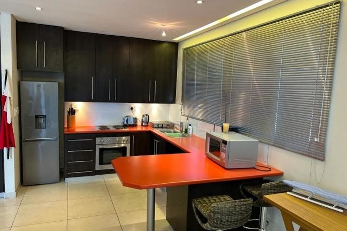 A functional kitchen featuring dark cabinetry, a vibrant red countertop, integrated oven and hob, and tiled flooring with a breakfast bar area.