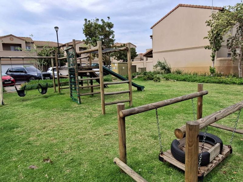 A communal garden area featuring a wooden playground structure and well-maintained lawn within a residential apartment complex.