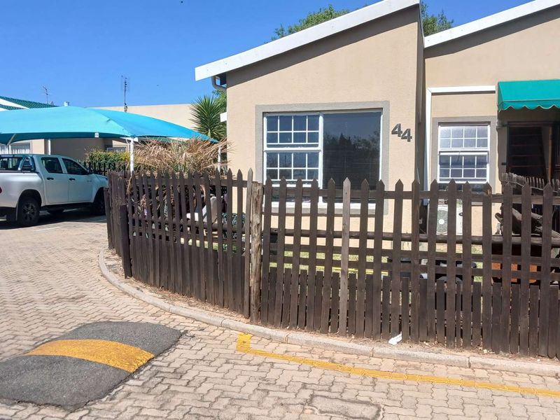 Front exterior view of the apartment unit featuring a private picket fence, paved driveway access, and a shaded parking area.
