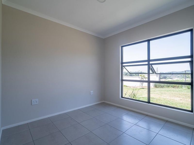 A bright, empty bedroom featuring neutral wall tones, tiled flooring, and a large window providing natural light and garden views.