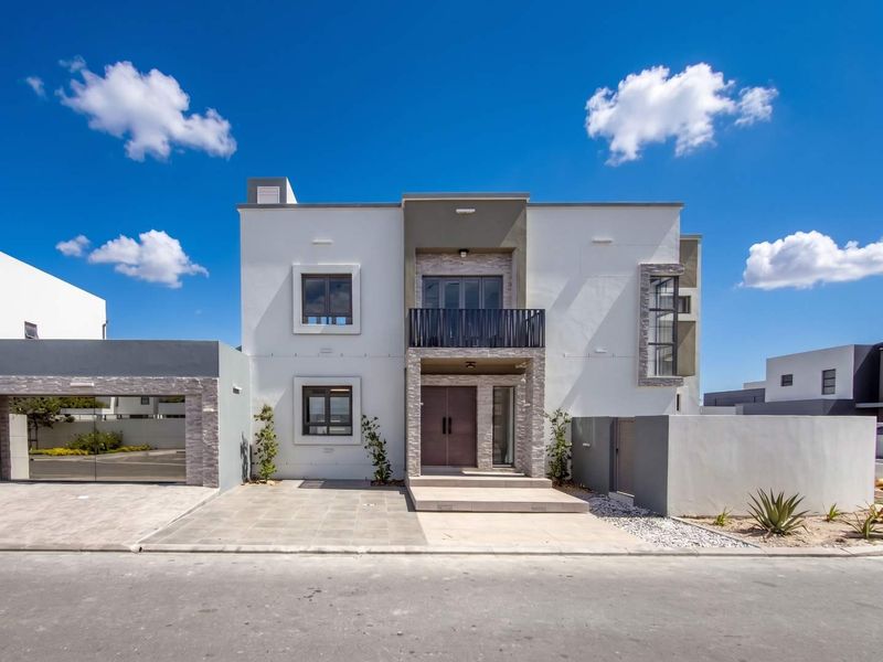 Modern double-story residential facade featuring stone cladding accents, a private balcony with metal railing, and a paved driveway leading to a double garage.