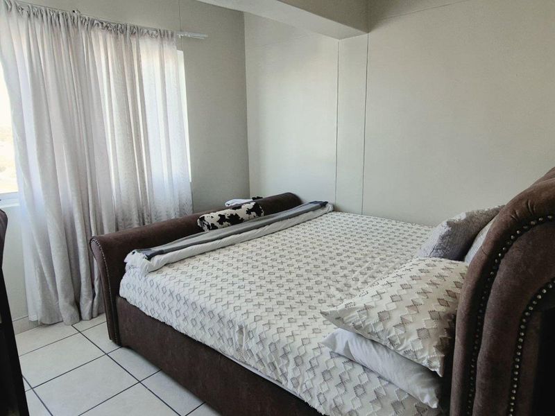 A compact bedroom featuring tiled flooring and a window with curtain tracks, providing a functional space for rest.