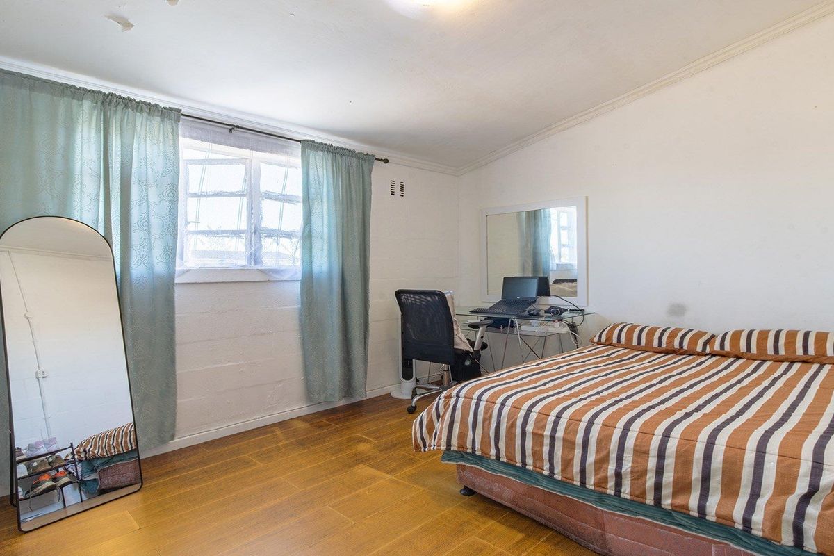 A functional bedroom featuring laminate flooring, coved ceilings, and a window, providing a comfortable space with potential for cosmetic updates.