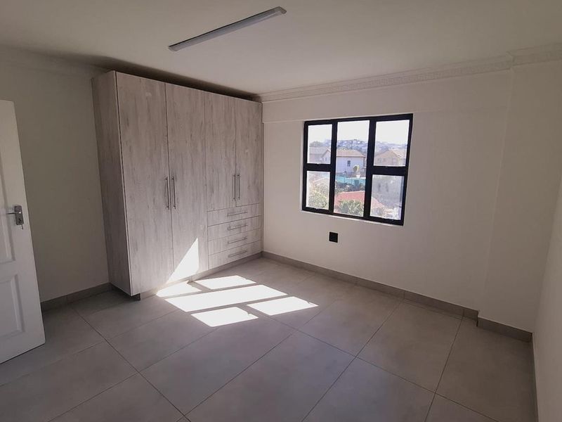 A bright, empty bedroom featuring neutral tiled flooring, a large built-in wardrobe with light wood finish, and a window providing natural light.