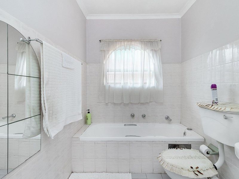 A functional bathroom featuring a built-in bathtub, tiled walls, and an arched window, offering a classic layout with potential for modern updates.