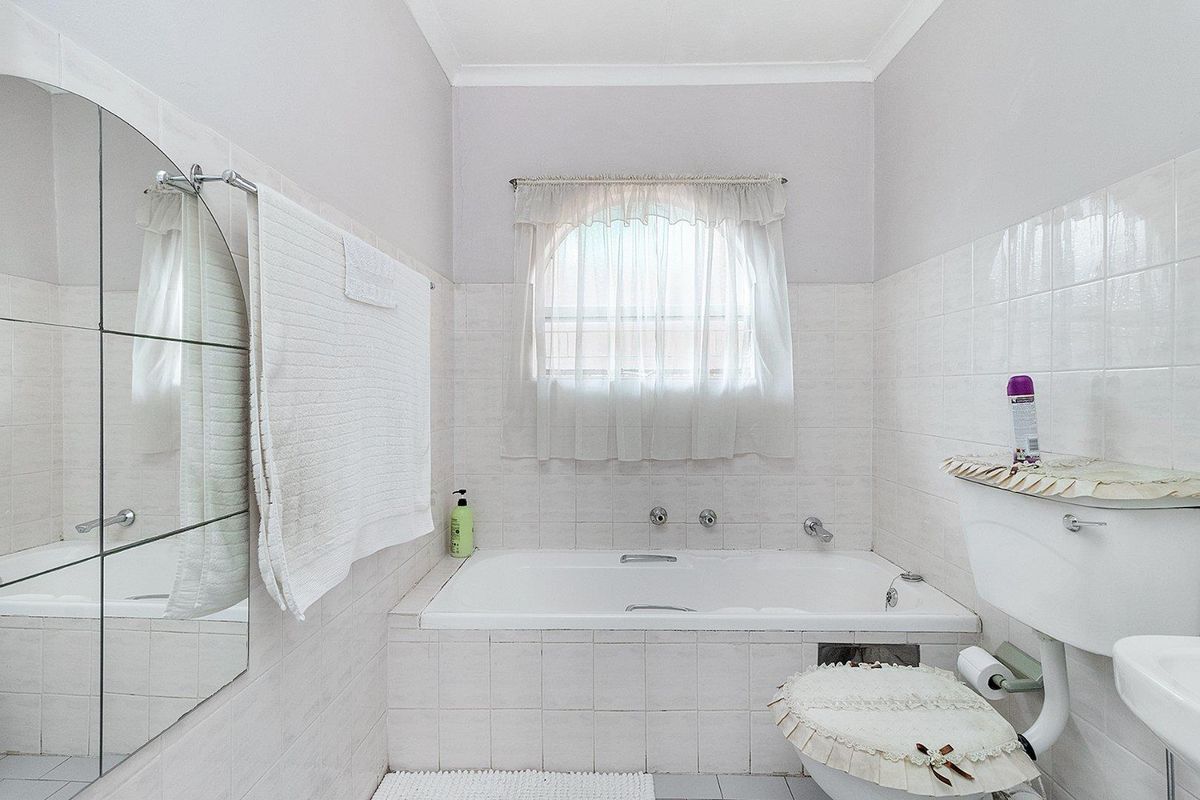A functional bathroom featuring a built-in bathtub, tiled walls, and an arched window, offering a classic layout with potential for modern updates.