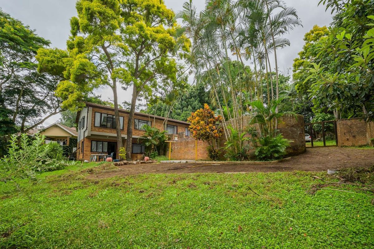 Rear view of a two-story brick house featuring mature trees, established garden landscaping, and a brick boundary wall.