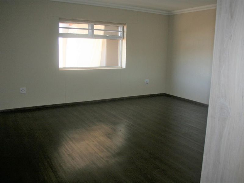 An empty bedroom featuring dark laminate flooring, neutral walls, and a sliding window, providing a blank canvas for personalization.