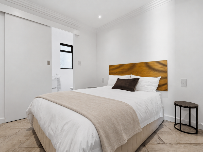 A modern, well-maintained bedroom featuring tiled flooring, crown molding, recessed lighting, and a sliding door leading to an en-suite bathroom.