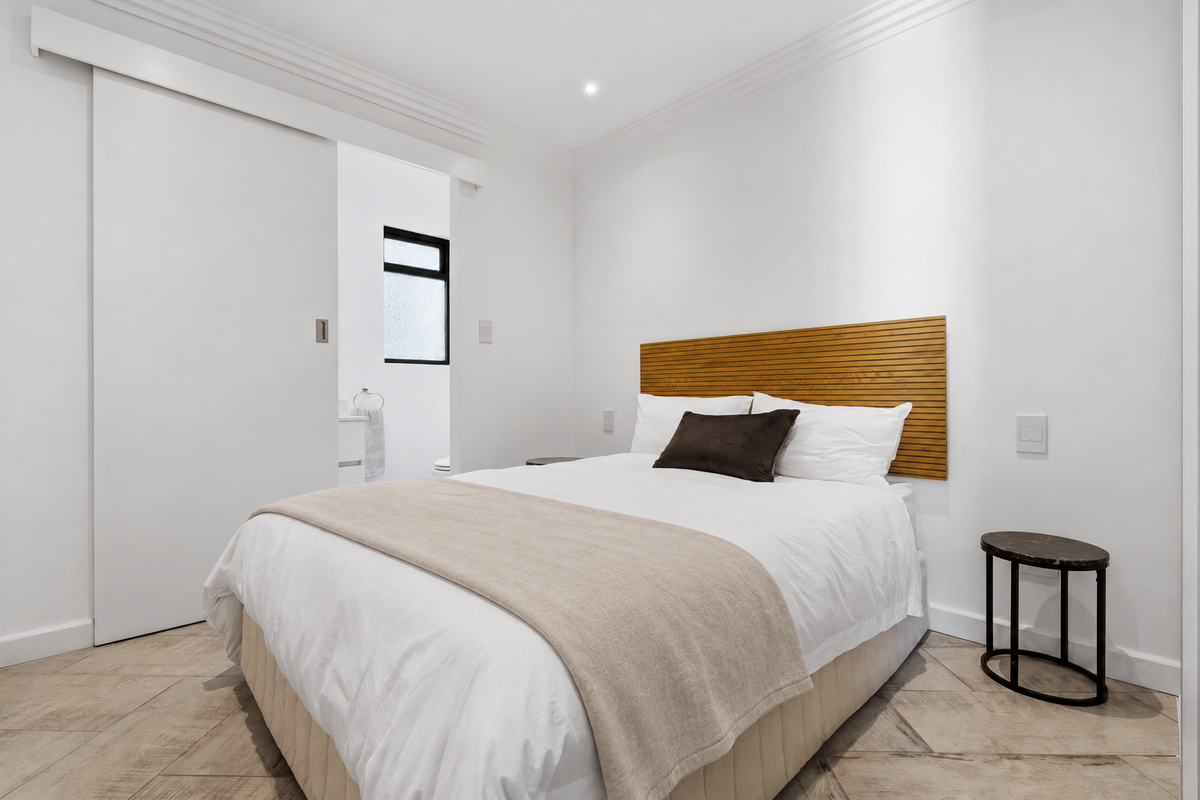 A modern, well-maintained bedroom featuring tiled flooring, crown molding, recessed lighting, and a sliding door leading to an en-suite bathroom.