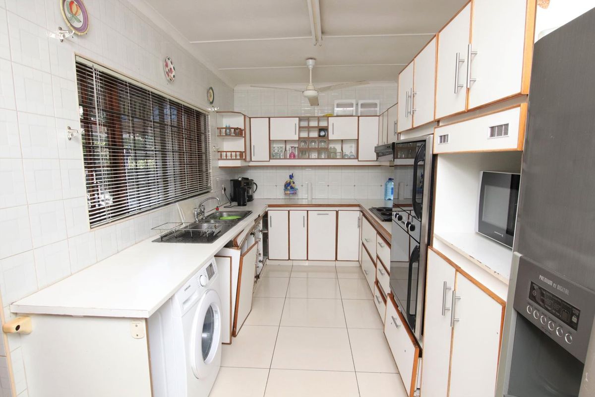 A functional kitchen featuring white cabinetry, tiled splashbacks, built-in oven, and integrated laundry space with tiled flooring.
