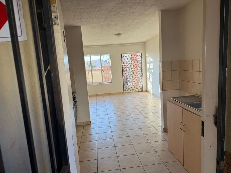 An open-plan living and kitchen area featuring tiled flooring, built-in cabinetry, and access to a balcony through a security gate.