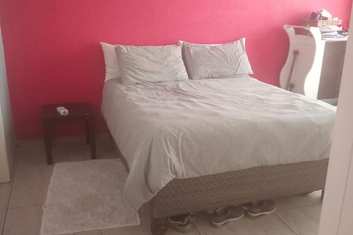 A bedroom featuring tiled flooring and a bright pink accent wall, providing a functional space with neutral base finishes.