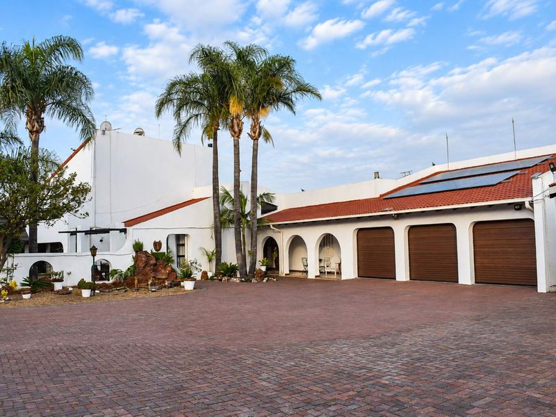 Spacious front exterior featuring a large paved driveway, triple garage, and a covered arched walkway with solar water heating panels on the roof.