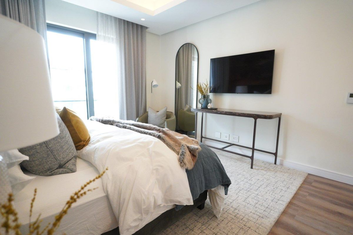 A well-appointed bedroom featuring modern recessed ceiling lighting, large sliding glass doors leading to a balcony, and wood-look flooring.