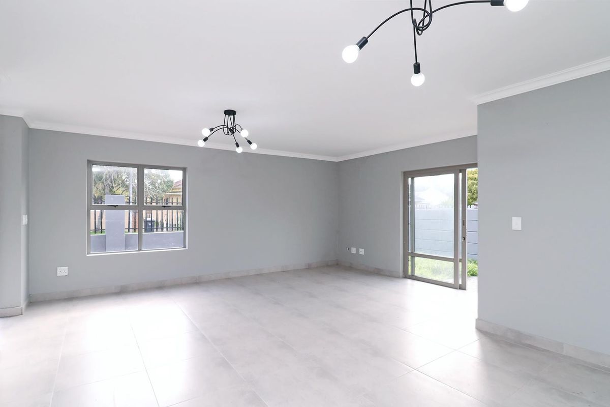 A bright, spacious, and empty living area featuring neutral grey walls, large tiled floors, modern lighting, and direct access to the outdoor space.