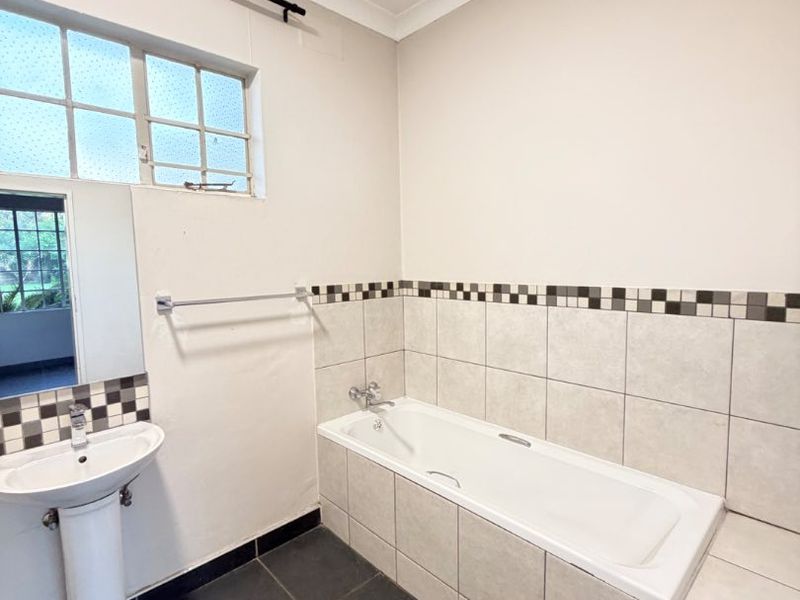 A functional bathroom featuring a built-in bathtub, pedestal basin, and neutral tiled finishes, offering a clean canvas for potential modern updates.