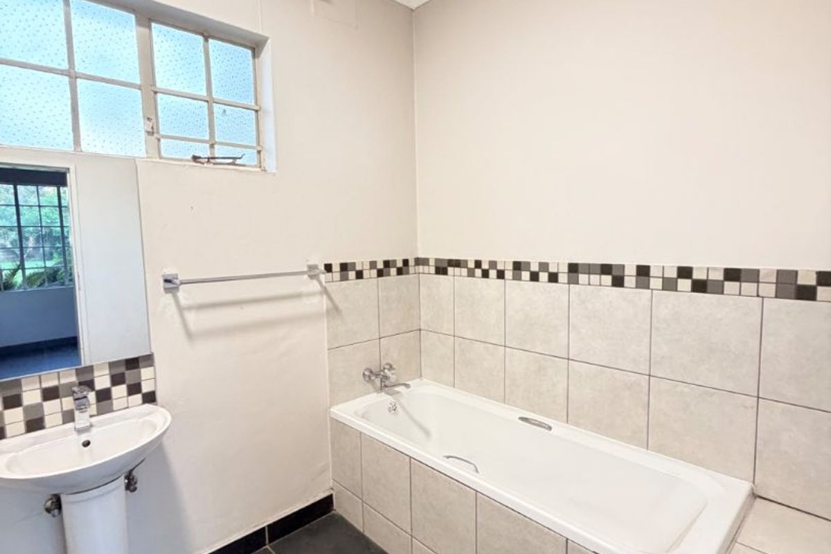 A functional bathroom featuring a built-in bathtub, pedestal basin, and neutral tiled finishes, offering a clean canvas for potential modern updates.