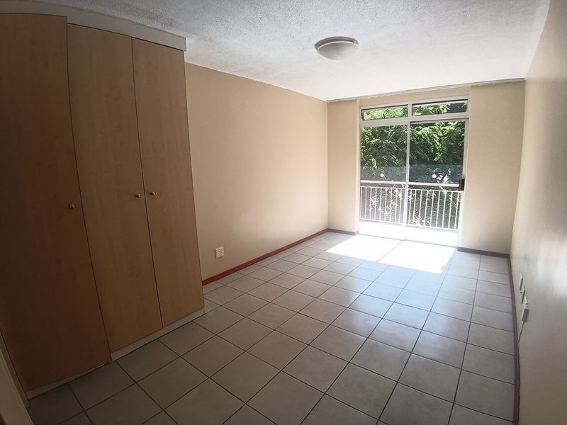 A bright, empty bedroom featuring neutral tiled flooring, built-in wooden cupboards, and a sliding glass door providing access to a balcony.