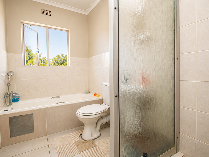 A functional bathroom featuring a built-in bathtub, separate shower enclosure, and tiled finishes, offering a practical layout with natural light from the window.