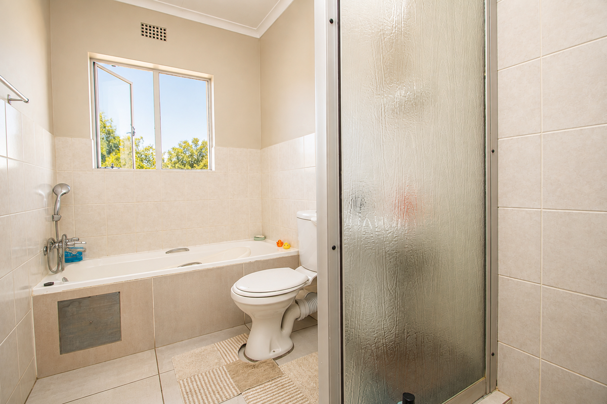 A functional bathroom featuring a built-in bathtub, separate shower enclosure, and tiled finishes, offering a practical layout with natural light from the window.