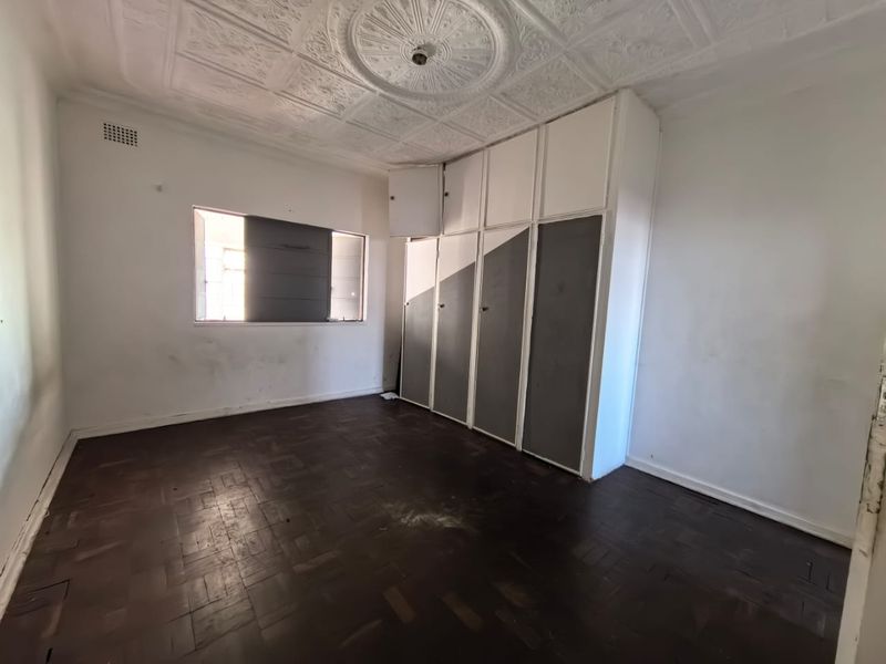 Empty bedroom featuring original parquet flooring, a decorative pressed metal ceiling with a central rose, and built-in storage cupboards.