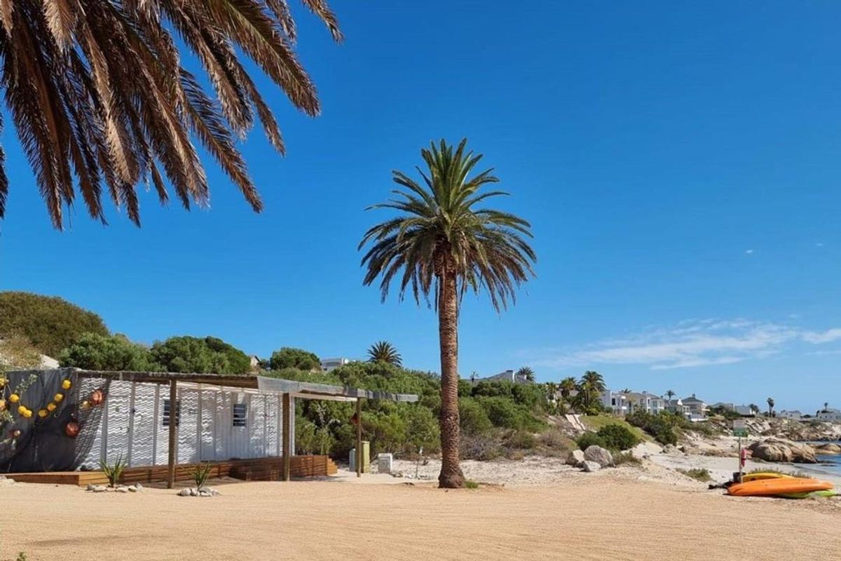 A coastal property featuring a wooden deck and covered patio area situated on a sandy beach with mature palm trees.