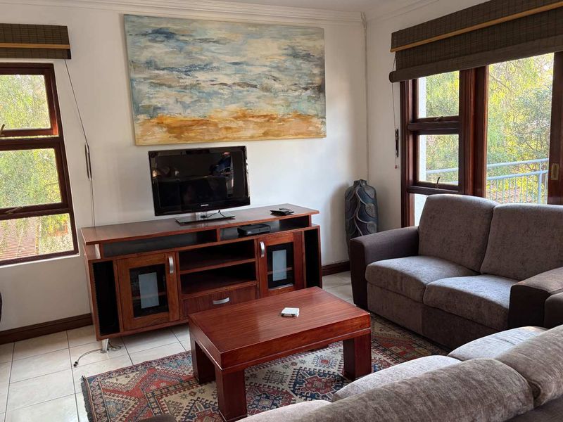 A comfortable living room featuring tiled flooring, timber-framed windows, and neutral wall finishes, providing a functional and well-lit space.