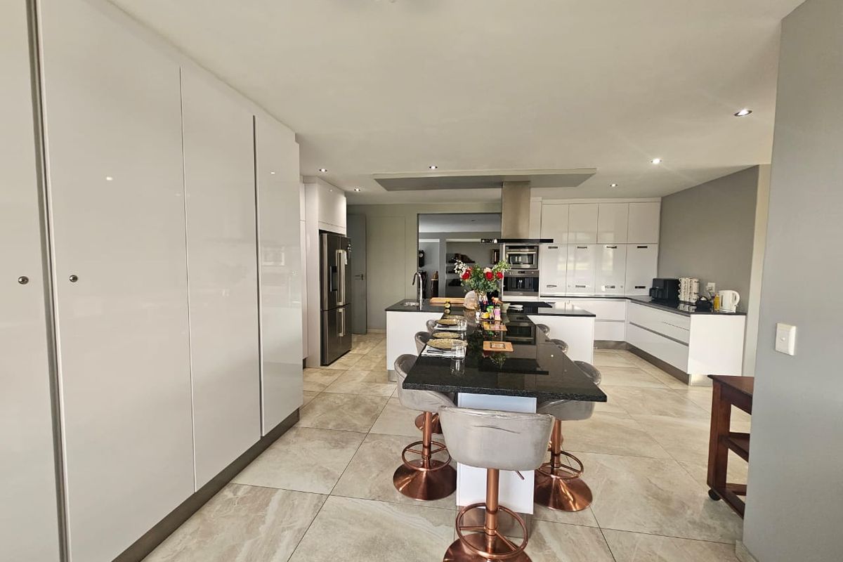 Modern open-plan kitchen featuring high-gloss cabinetry, a central island with stone countertop, integrated appliances, and large format floor tiles.