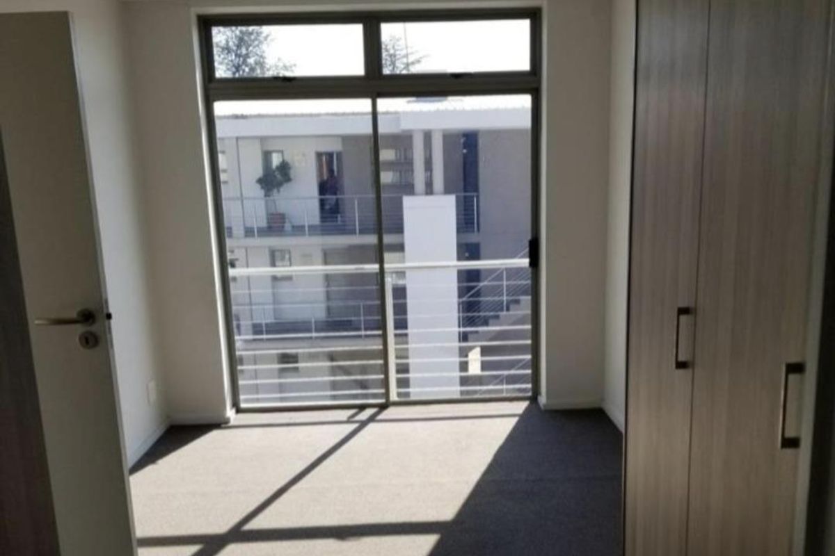A bright, empty bedroom featuring neutral carpeting, built-in cupboards, and a sliding glass door leading to a balcony.