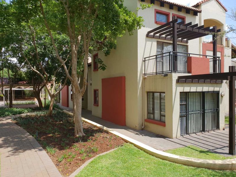 Exterior view of an apartment building featuring a balcony with a pergola, security bars on ground floor windows, and landscaped garden area.