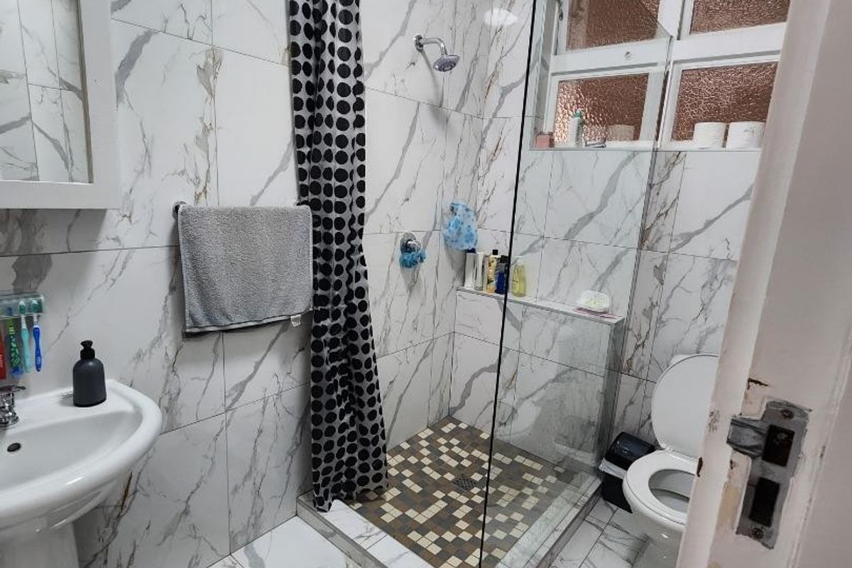 A modern bathroom featuring marble-look wall and floor tiles, a glass-enclosed shower with mosaic flooring, a pedestal basin, and a toilet.