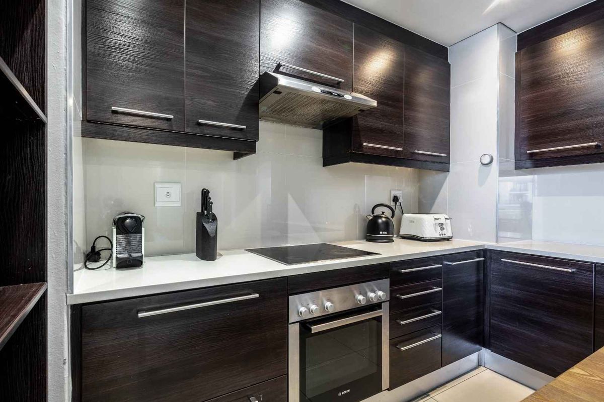 Modern kitchen featuring dark wood cabinetry, stone countertops, a built-in oven, electric cooktop, and stainless steel extractor fan.