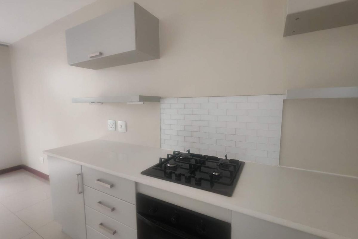 Modern kitchen featuring light grey cabinetry, white stone countertops, a built-in gas hob, and a subway tile backsplash.