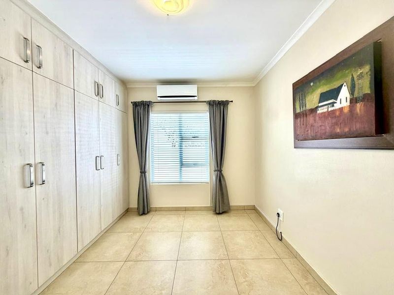 A clean, well-maintained bedroom featuring extensive built-in cabinetry, tiled flooring, and a wall-mounted air conditioning unit.