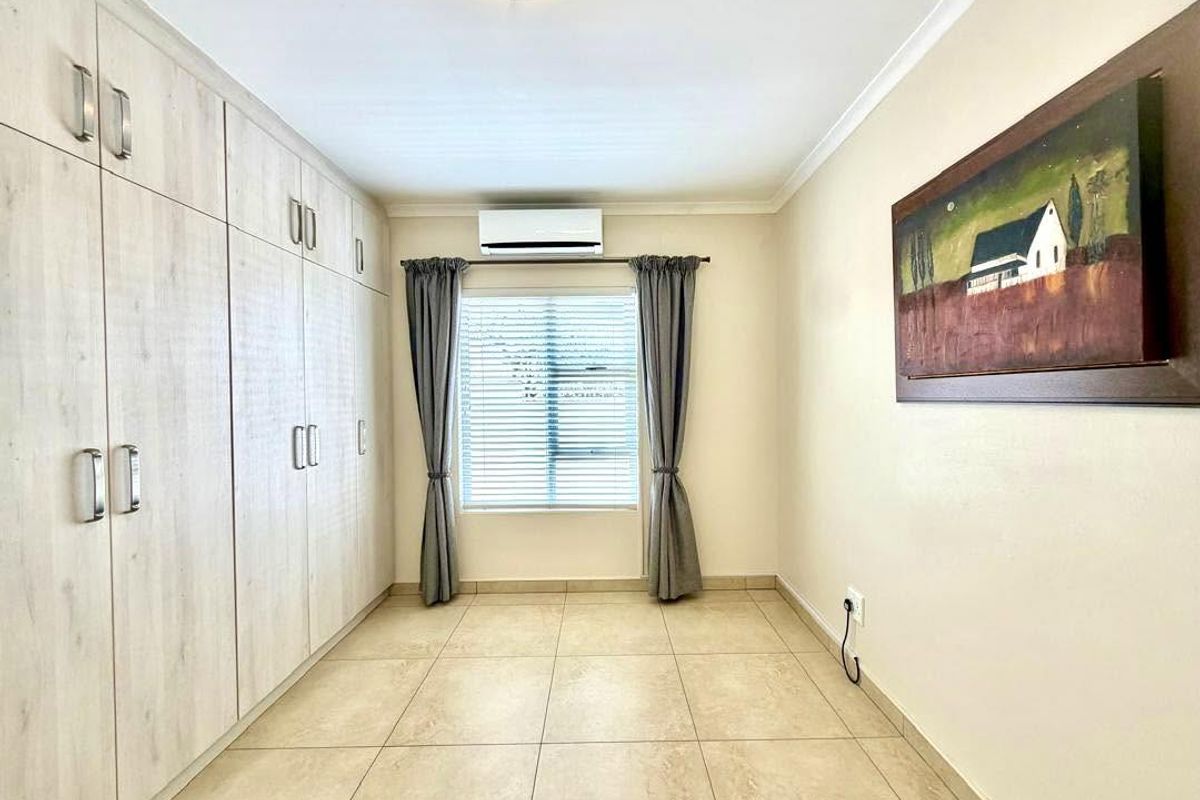 A clean, well-maintained bedroom featuring extensive built-in cabinetry, tiled flooring, and a wall-mounted air conditioning unit.