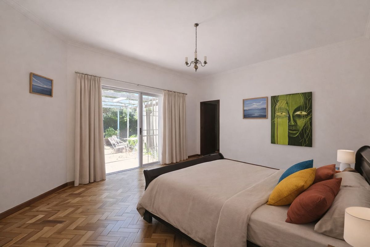 Spacious bedroom featuring classic herringbone parquet flooring, a central chandelier, and sliding glass doors providing direct access to an outdoor patio area.
