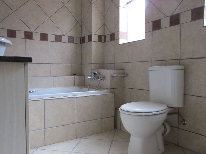 A functional bathroom featuring a built-in bathtub, toilet, and neutral tiled finishes throughout.