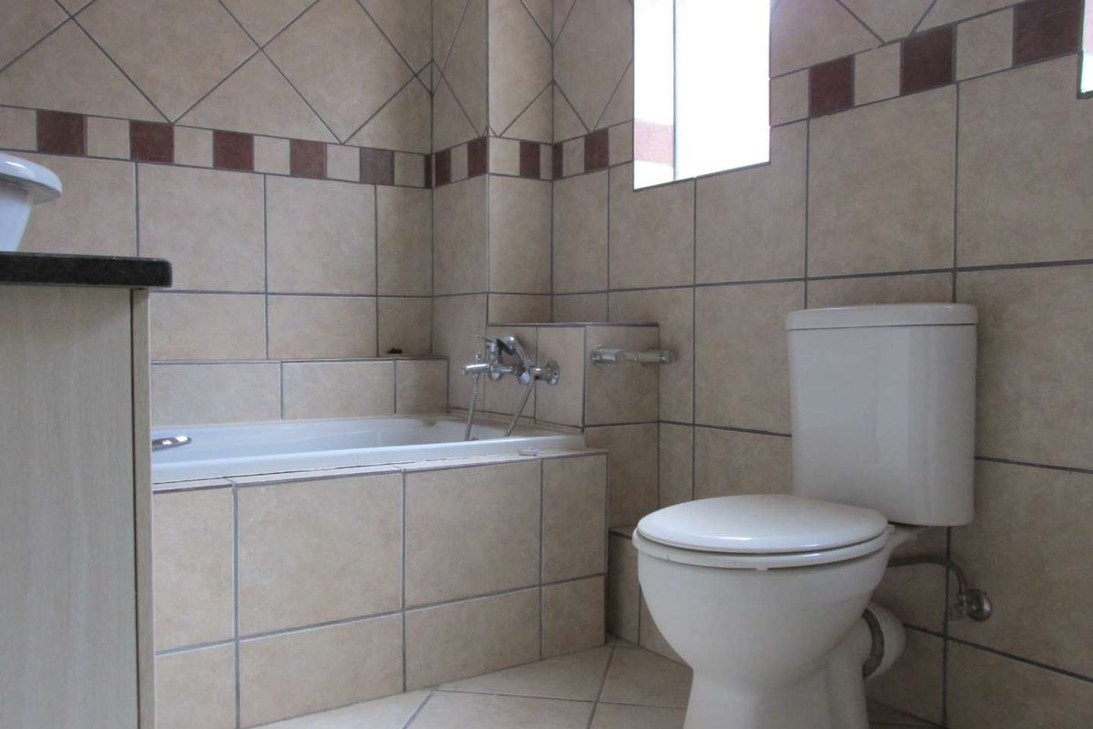 A functional bathroom featuring a built-in bathtub, toilet, and neutral tiled finishes throughout.