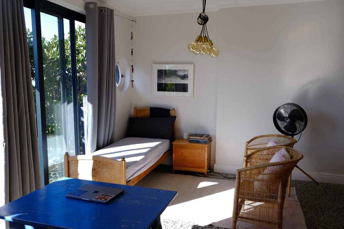 A bright bedroom featuring large sliding glass doors that provide access to the outdoors, complemented by a unique circular window and modern pendant lighting.