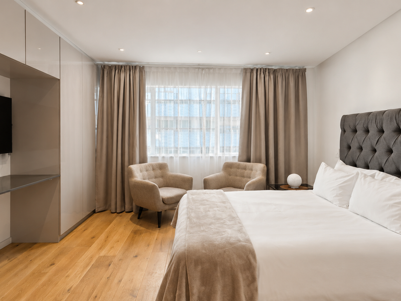 A well-appointed bedroom featuring high-quality hardwood flooring, extensive built-in cabinetry with an integrated desk, and recessed ceiling lighting.