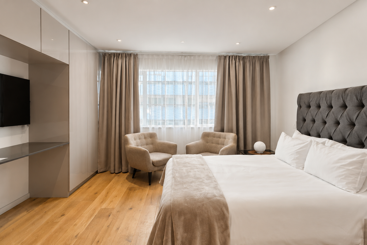 A well-appointed bedroom featuring high-quality hardwood flooring, extensive built-in cabinetry with an integrated desk, and recessed ceiling lighting.
