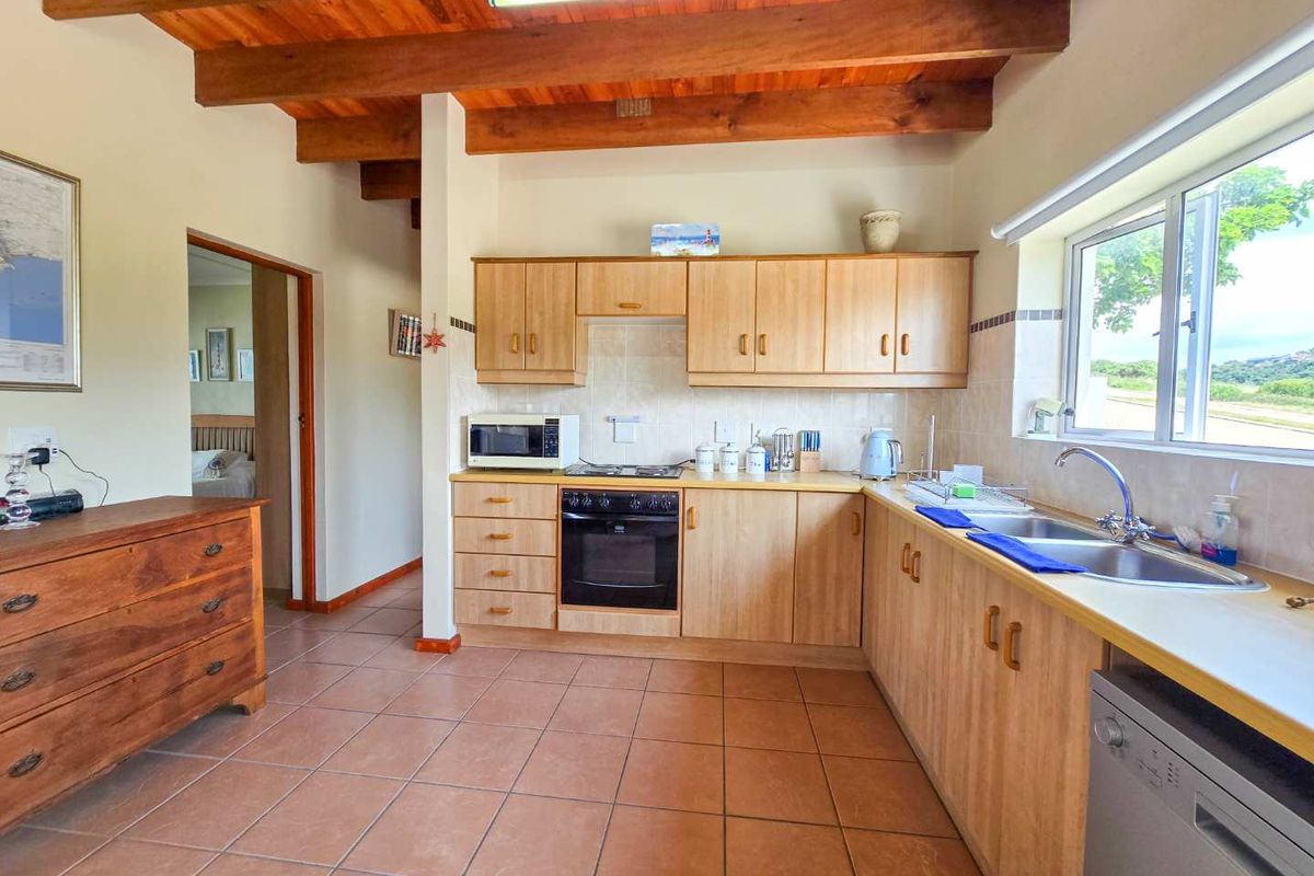 A functional kitchen featuring light wood cabinetry, exposed timber ceiling beams, tiled flooring, and a built-in oven with a hob.