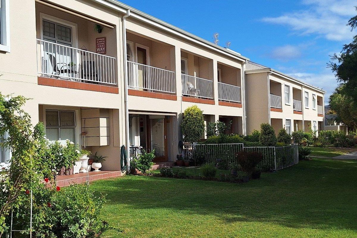 Exterior view of a multi-story apartment complex featuring private balconies, ground-floor patios, and well-maintained communal garden areas.