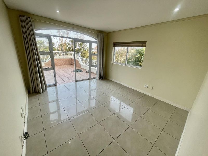 Spacious living area featuring neutral tiled flooring, recessed lighting, and large sliding glass doors providing direct access to an outdoor patio area.