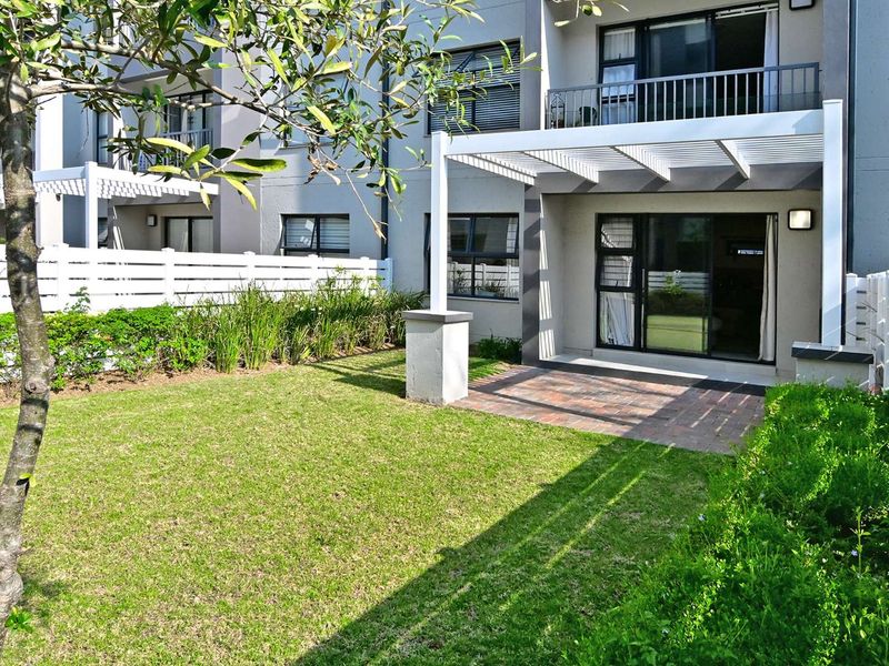 A well-maintained rear garden featuring a paved patio area with a pergola, sliding glass doors leading to the interior, and a private lawn.